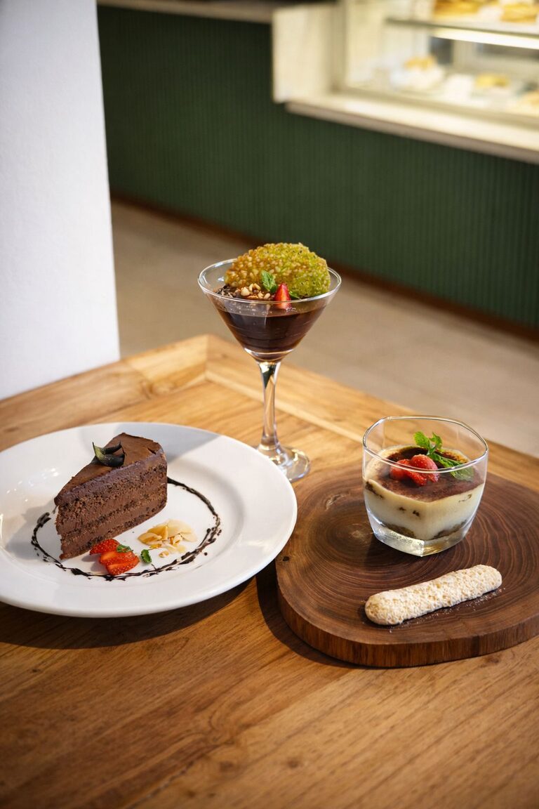 Three desserts together: a chocolate layer cake slice, a glass of chocolate mousse with a caramel tuile, and a tiramisu.
