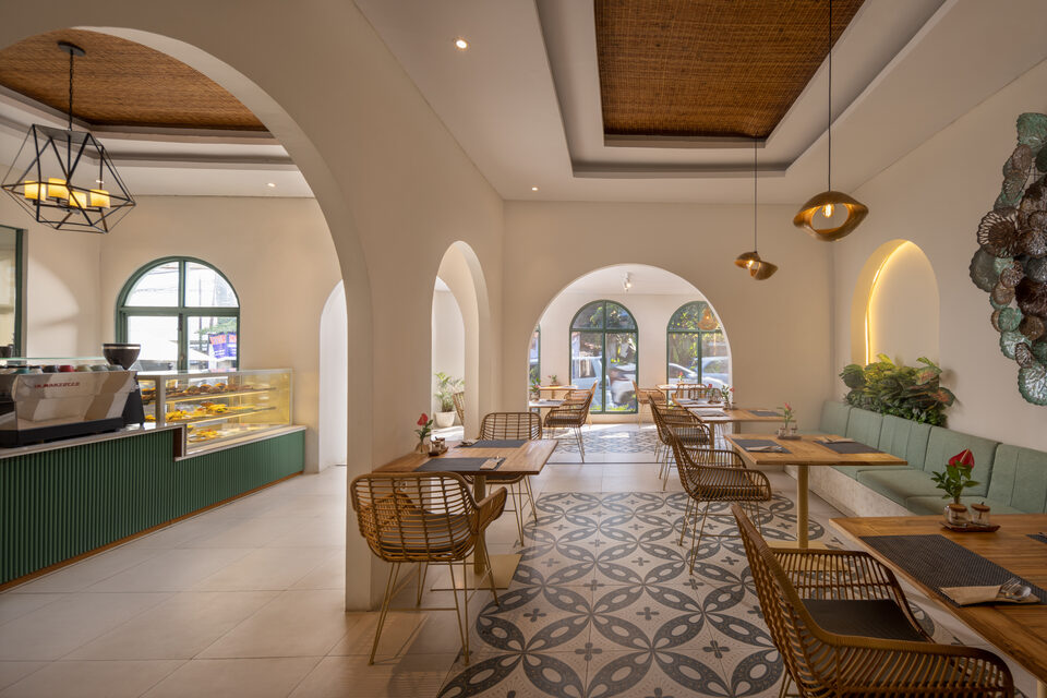 The indoor dining room in daylight, with white plaster arches and brass pendant lights.