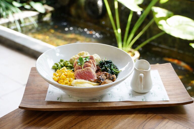 A tuna poke bowl on a teak tray beside the koi pond, with a small jug of soy ginger dressing.