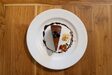 Overhead view of a chocolate layer cake slice with a ring of chocolate sauce, flaked almonds and a strawberry.